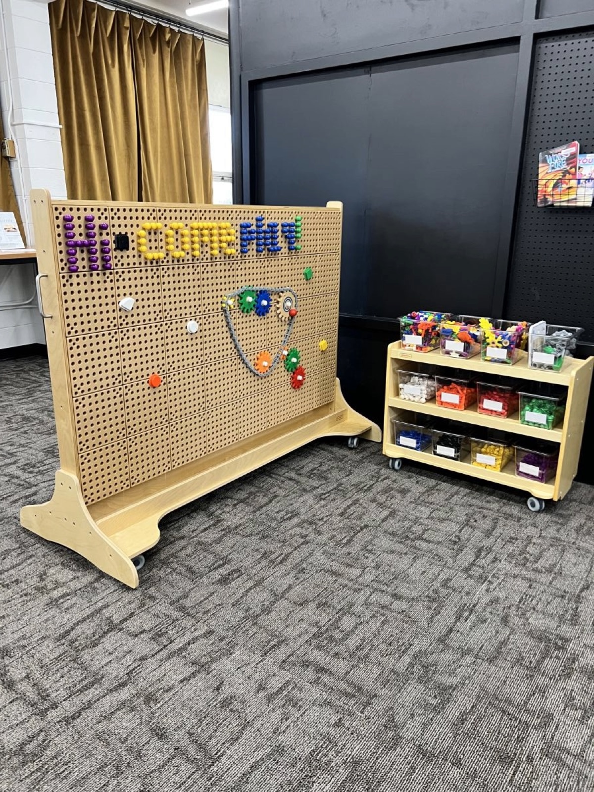 Pegboard activity wall and building-toy cart in the children's area